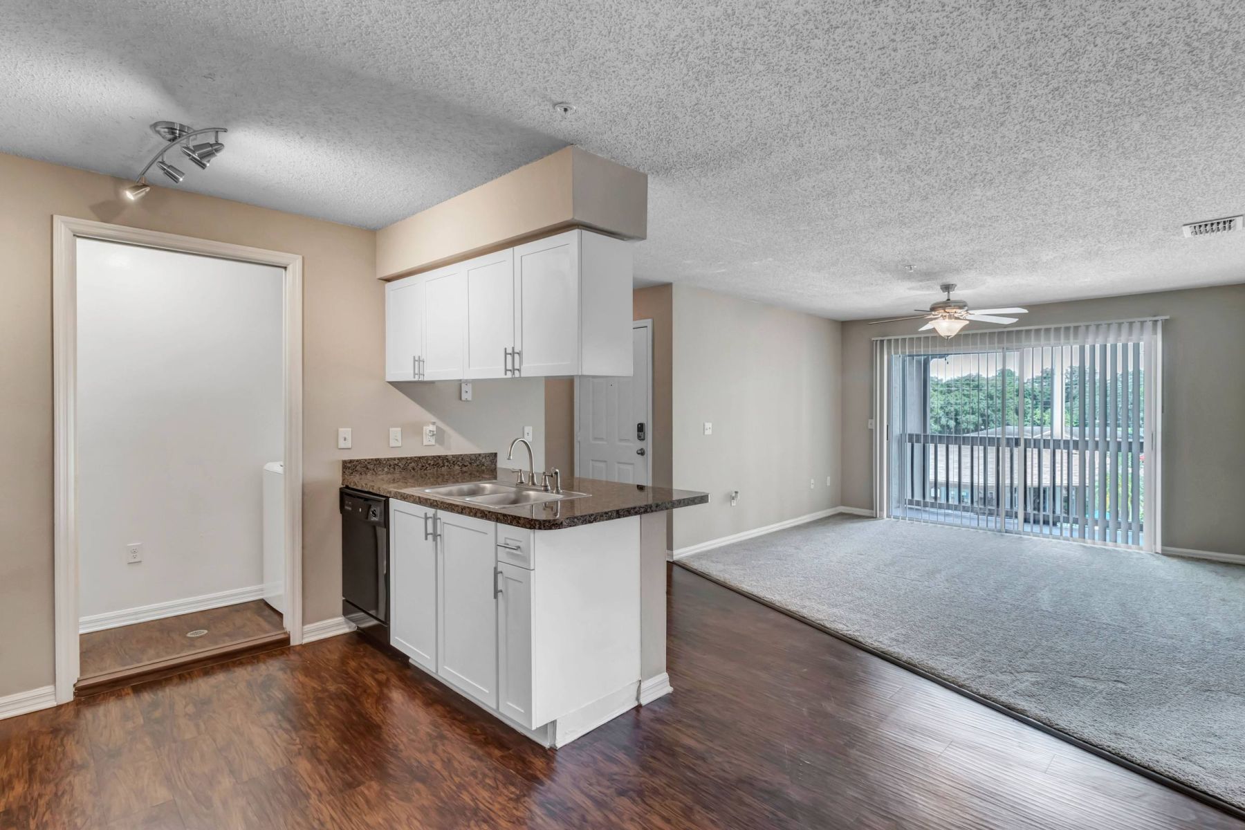 Empty room with wood floors, ceiling fan, and sliding glass door leading to a patio with vertical blinds at Apex West Midown.